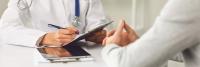 Doctor Writing Prescription While Patient Sitting At Hospital